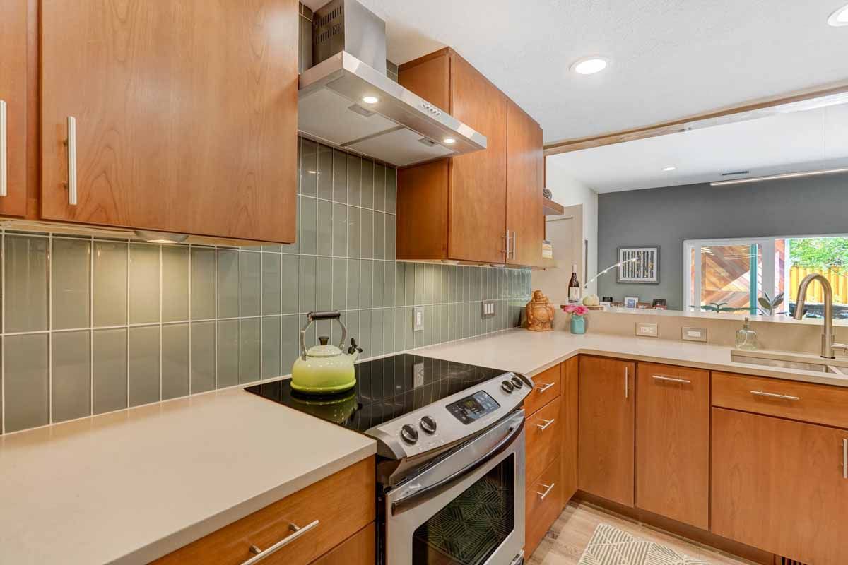 Modern kitchen with wooden cabinets, stainless stove, gray backsplash, and a large window over the sink