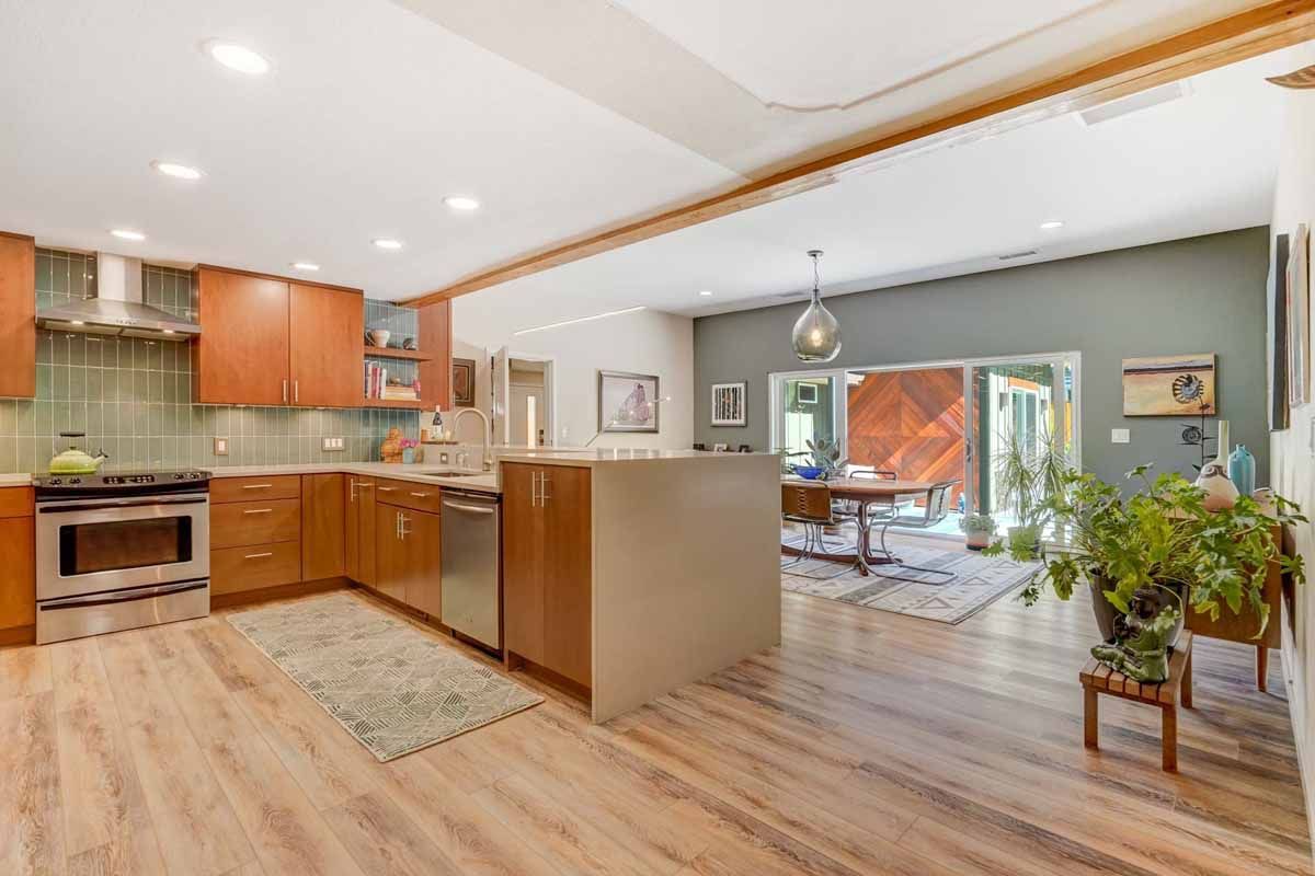 Open-plan kitchen and living area with wood floors, orange cabinets, and large windows looking onto a patio.