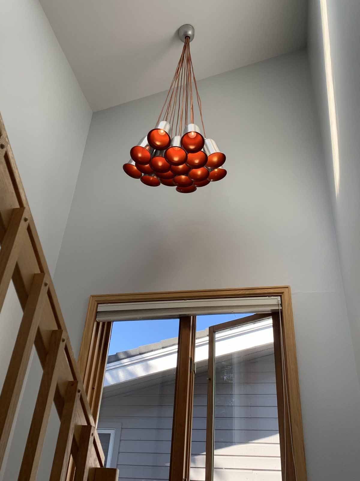 Cluster of red fruits or ornaments hanging from the ceiling in a tall stairwell by a window.