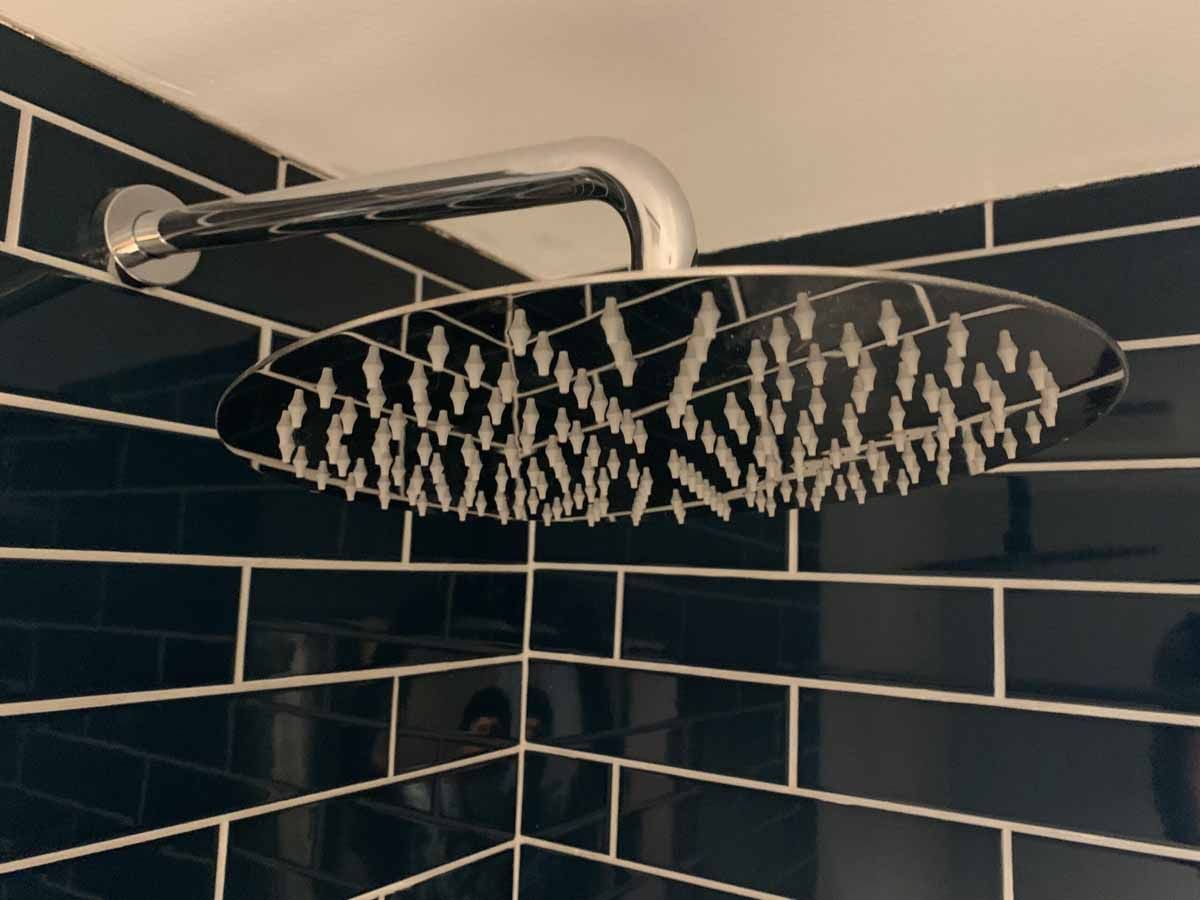 Black-tiled shower corner with a large chrome rainfall showerhead and matching overhead pipe
