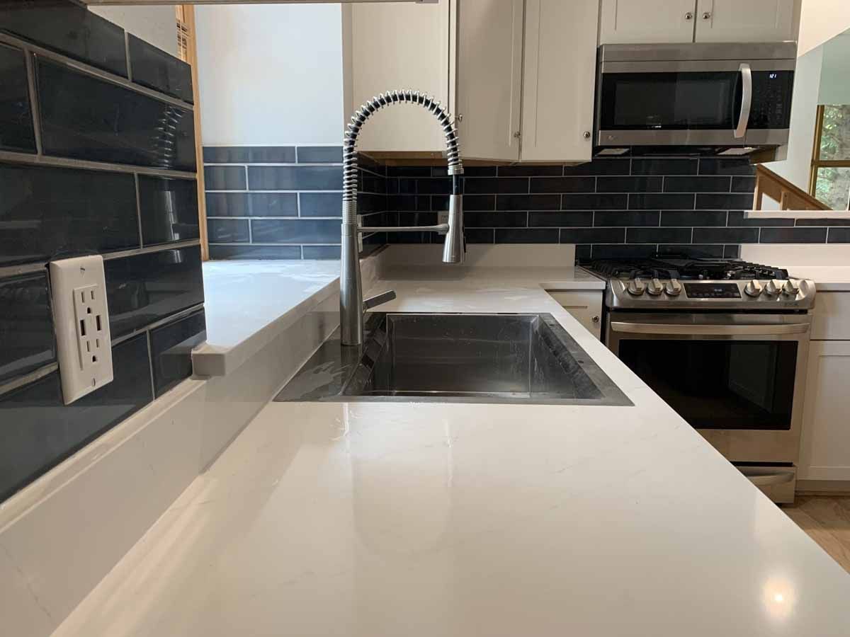 Modern kitchen with white island, sink, black tile backsplash, and stainless steel appliances