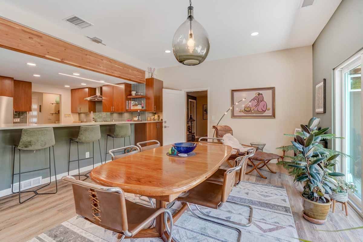 Bright dining room with wooden table, glass barstools, pendant light, and open kitchen.