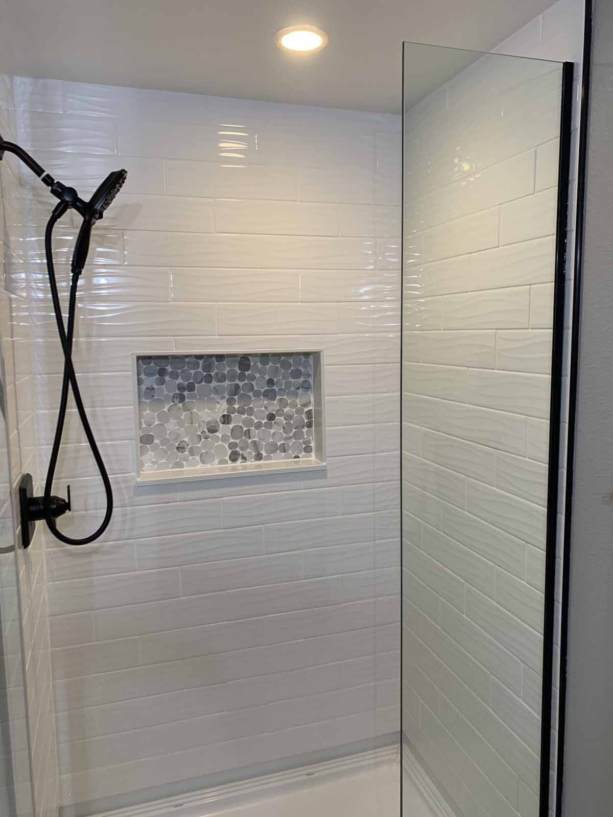 Modern shower with glass door, black showerhead, and mosaic tile niche under a recessed light
