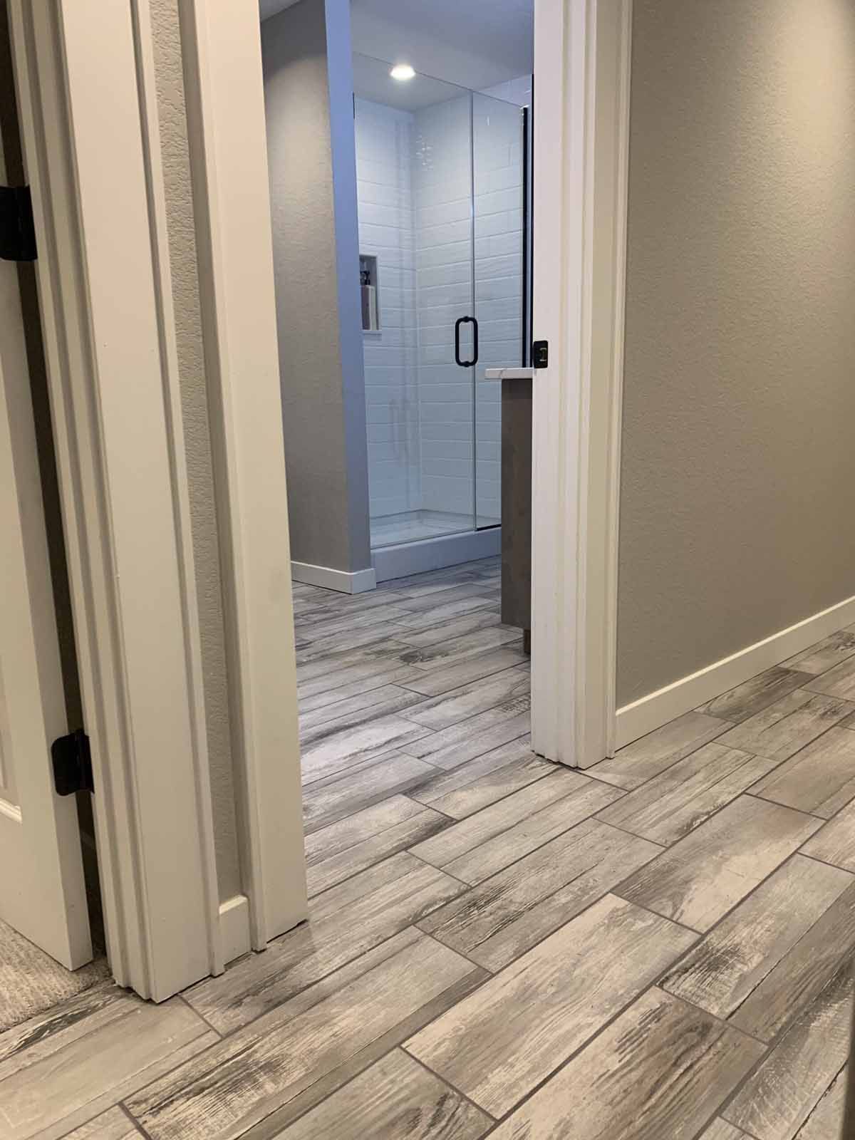 Modern hallway with light wood floors and a glass-tiled shower visible through an open doorway