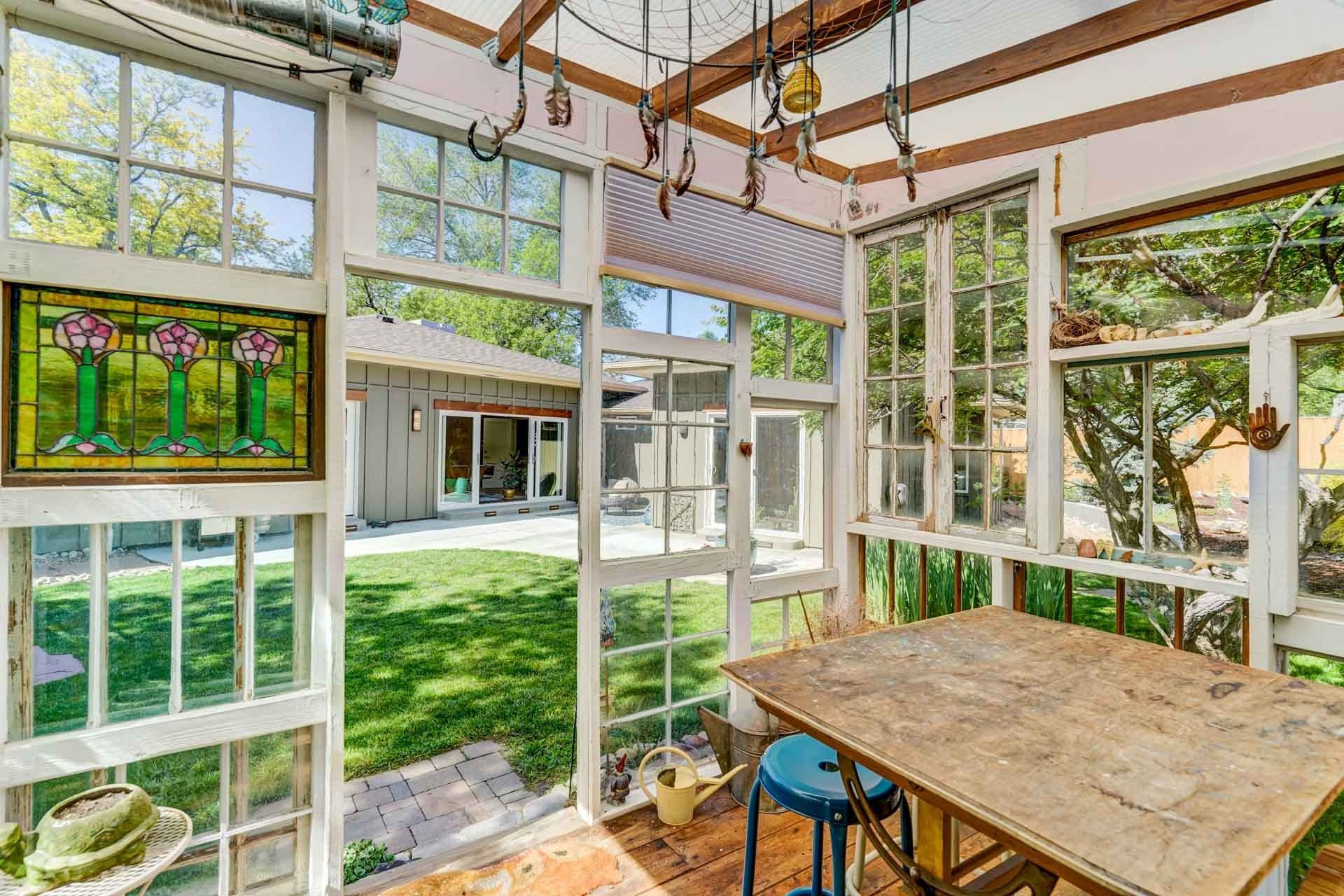 Sunlit porch with stained-glass windows, white framing, and a wooden table overlooking a green courtyard.