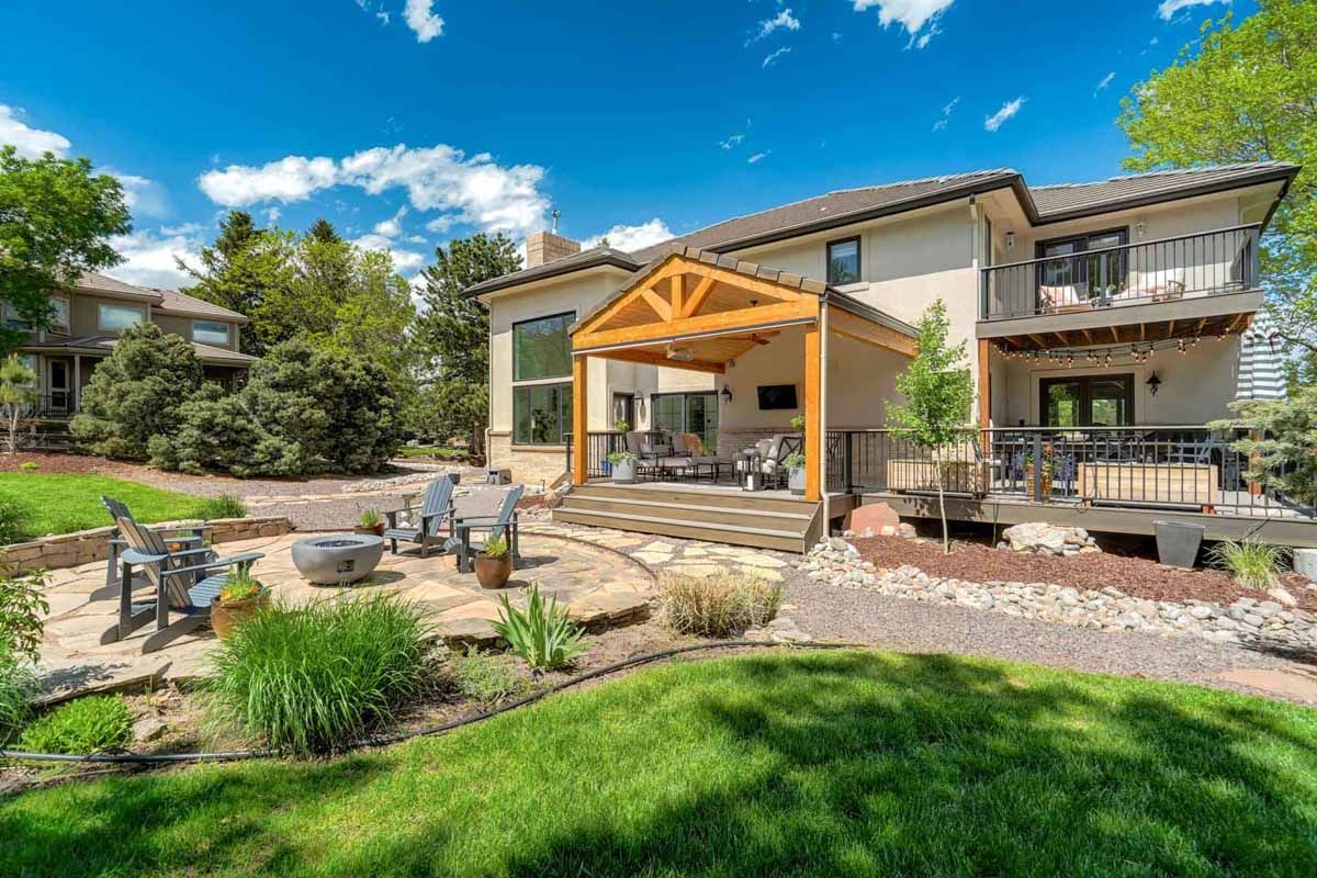 Modern house with covered patio, stone seating area, and landscaped backyard under a blue sky