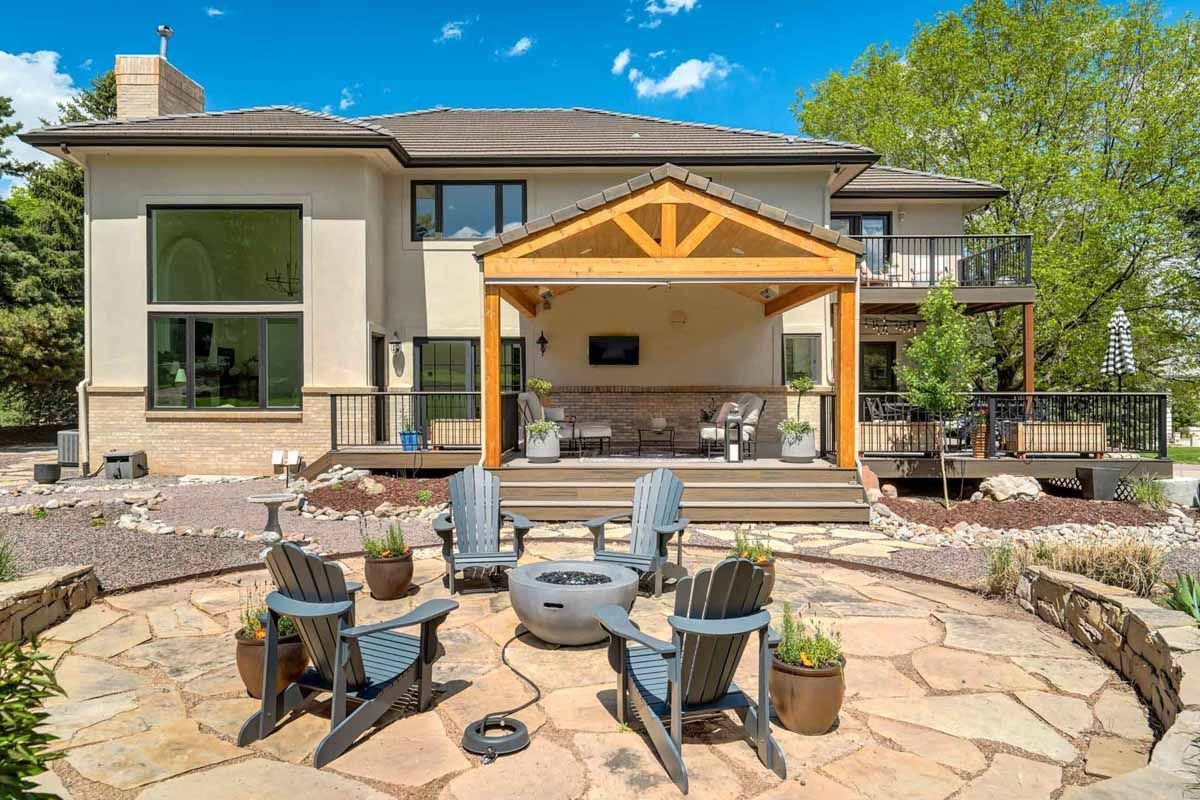 Backyard patio with stone fire pit, seating area, and covered outdoor kitchen beside a modern house