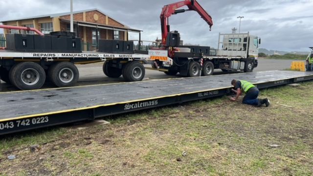 A man is kneeling next to a truck that is being towed by a crane.