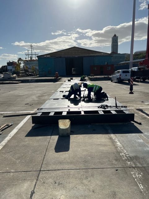 Two men are working on a large piece of metal in a parking lot