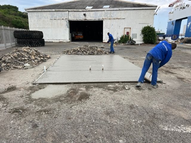 Two men are working on a concrete floor in front of a building.