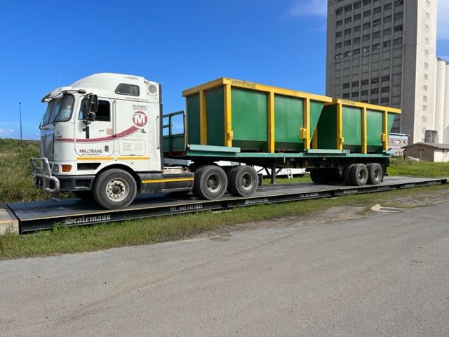 A white semi truck with a green trailer is sitting on a scale.
