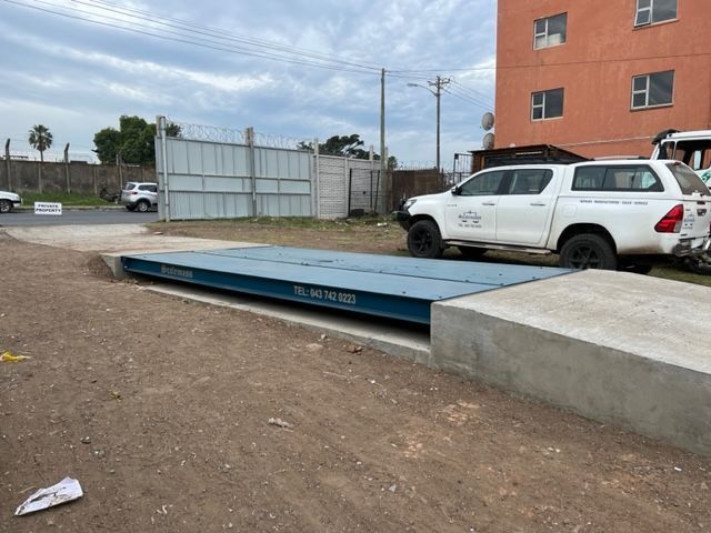 A white truck is parked on a scale in front of a building.