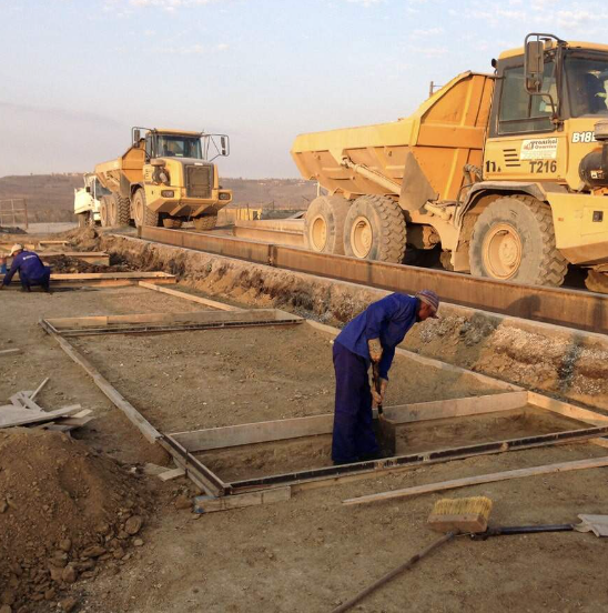 A man is digging in the dirt in front of a yellow dump truck that says volvo