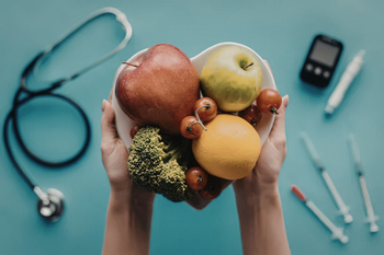 Hands holding assorted fruits and vegetables on a teal background with medical tools around them
