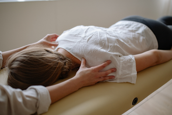 Person lying face down on a massage table while a therapist supports their head and shoulders