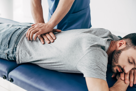 Massage therapist pressing on a man's back as he lies face down on a treatment table