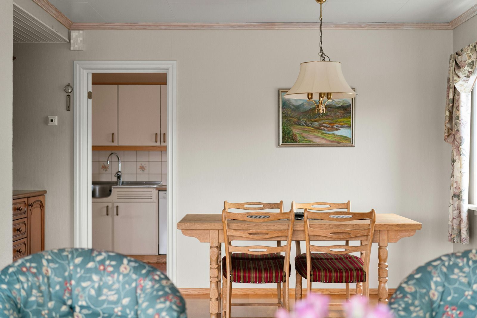 Dining room with wooden table, chairs, and painting; kitchen doorway visible.