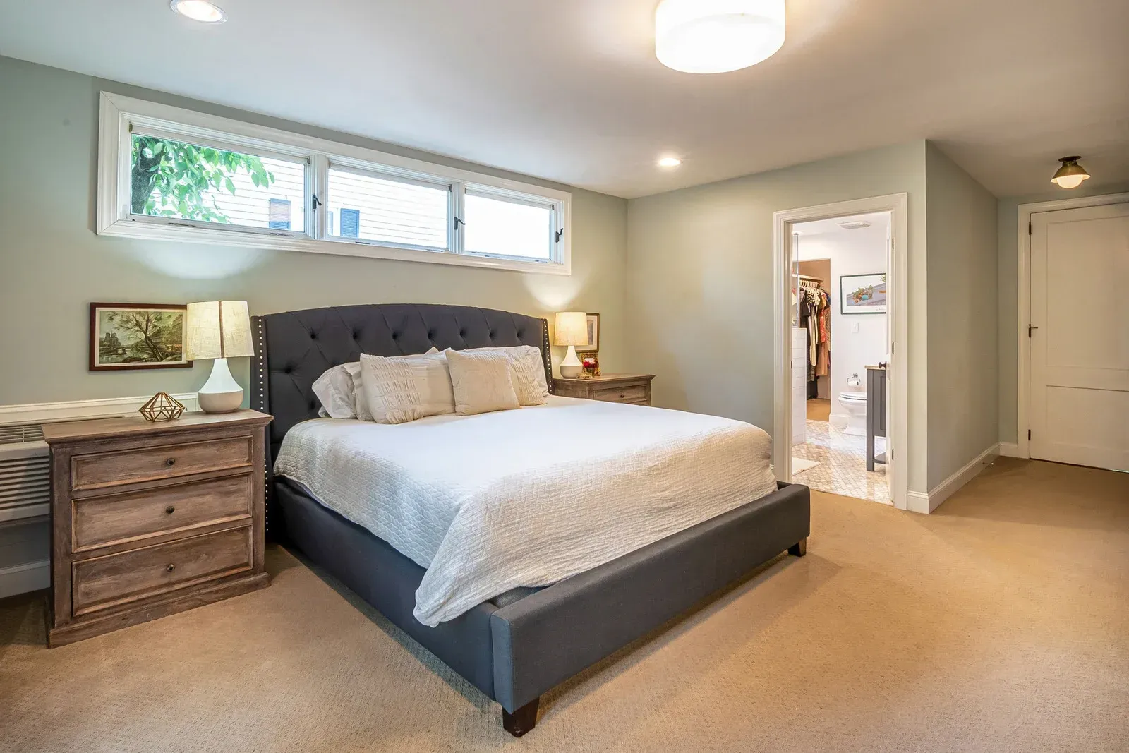 Bedroom with gray tufted bed, wood nightstands, and pale green walls.
