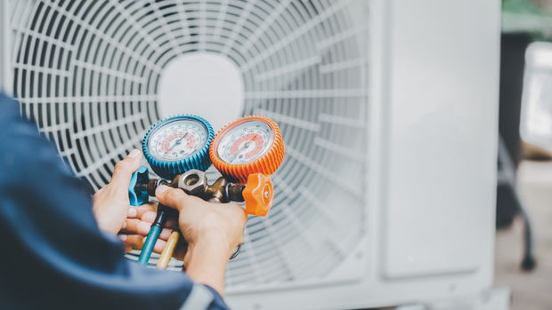 A man is working on an air conditioner with two gauges.