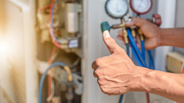 A man is giving a thumbs up while working on an air conditioner.