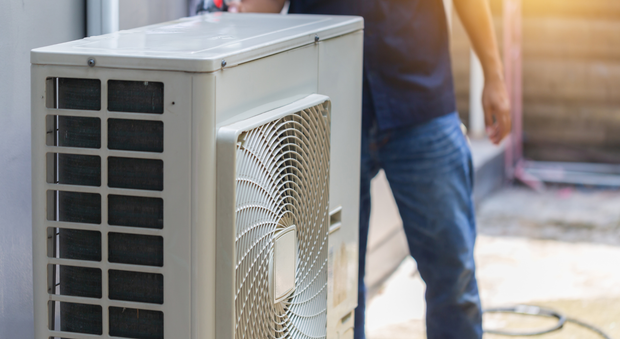 A man is standing next to a large air conditioner outside of a building.