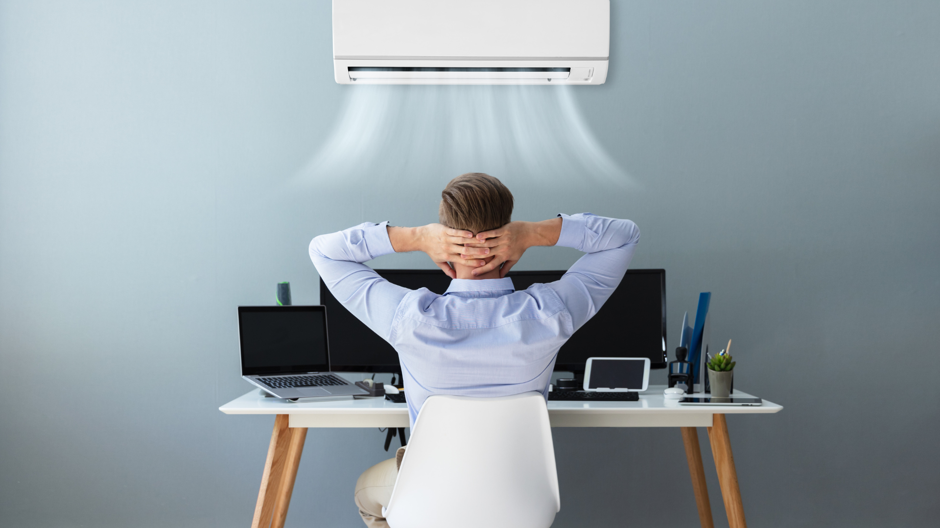 A man is sitting at a desk under an air conditioner.