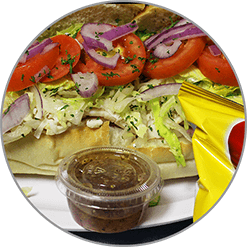 A sandwich with tomatoes , lettuce , onions and a dipping sauce on a plate.