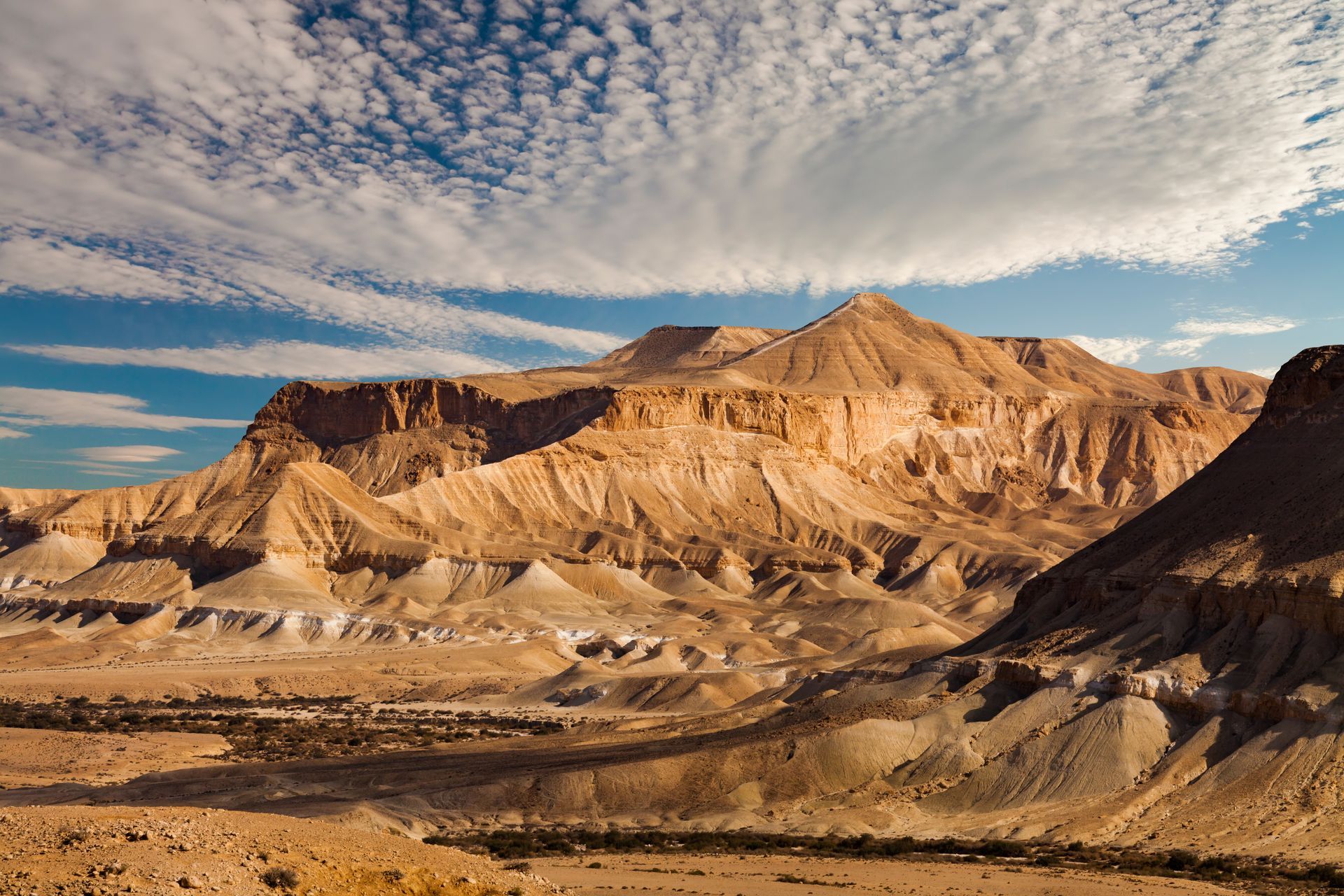 Brown mountains and desert under a blue sky with streaky clouds.