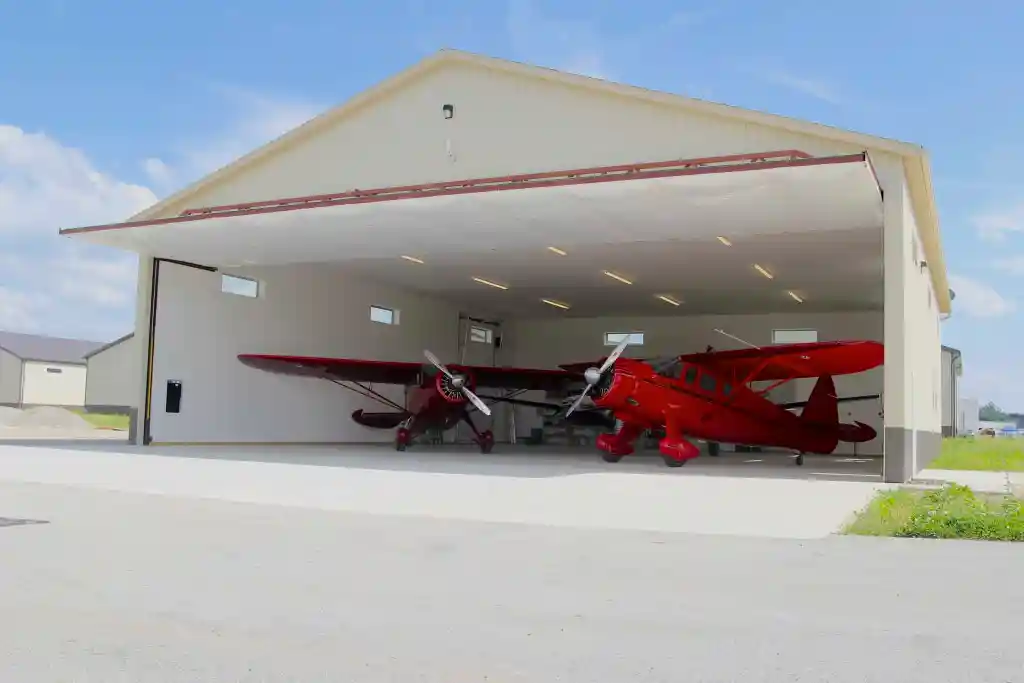 two red airplanes are parked in a hangar with the door open .