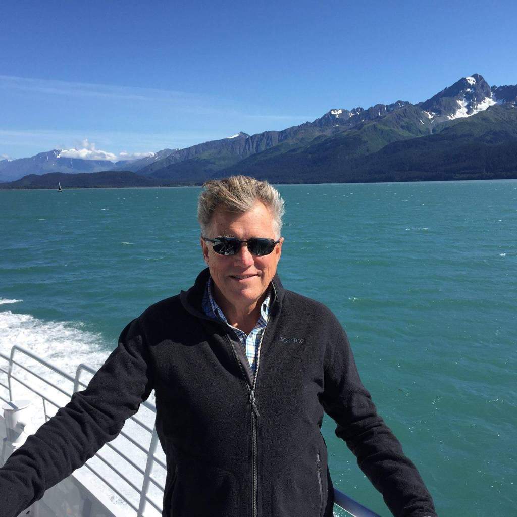 a man wearing sunglasses is standing on a boat with mountains in the background