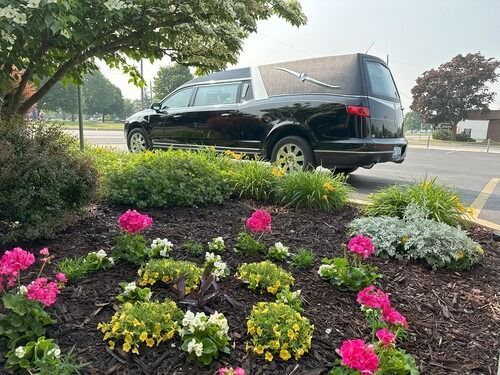 Black hearse parked near a flower garden at a cemetery.