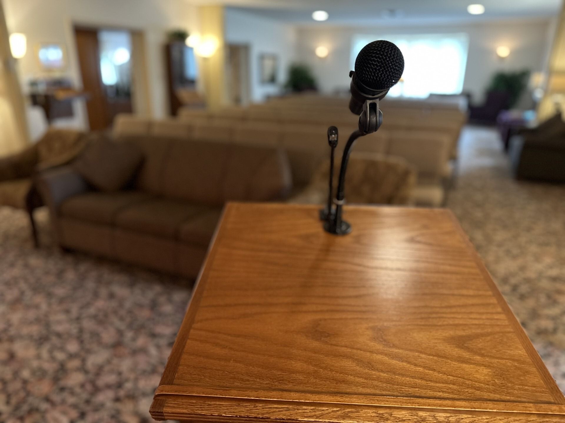 Microphone on a wooden podium, with blurred couches and a waiting area in the background.