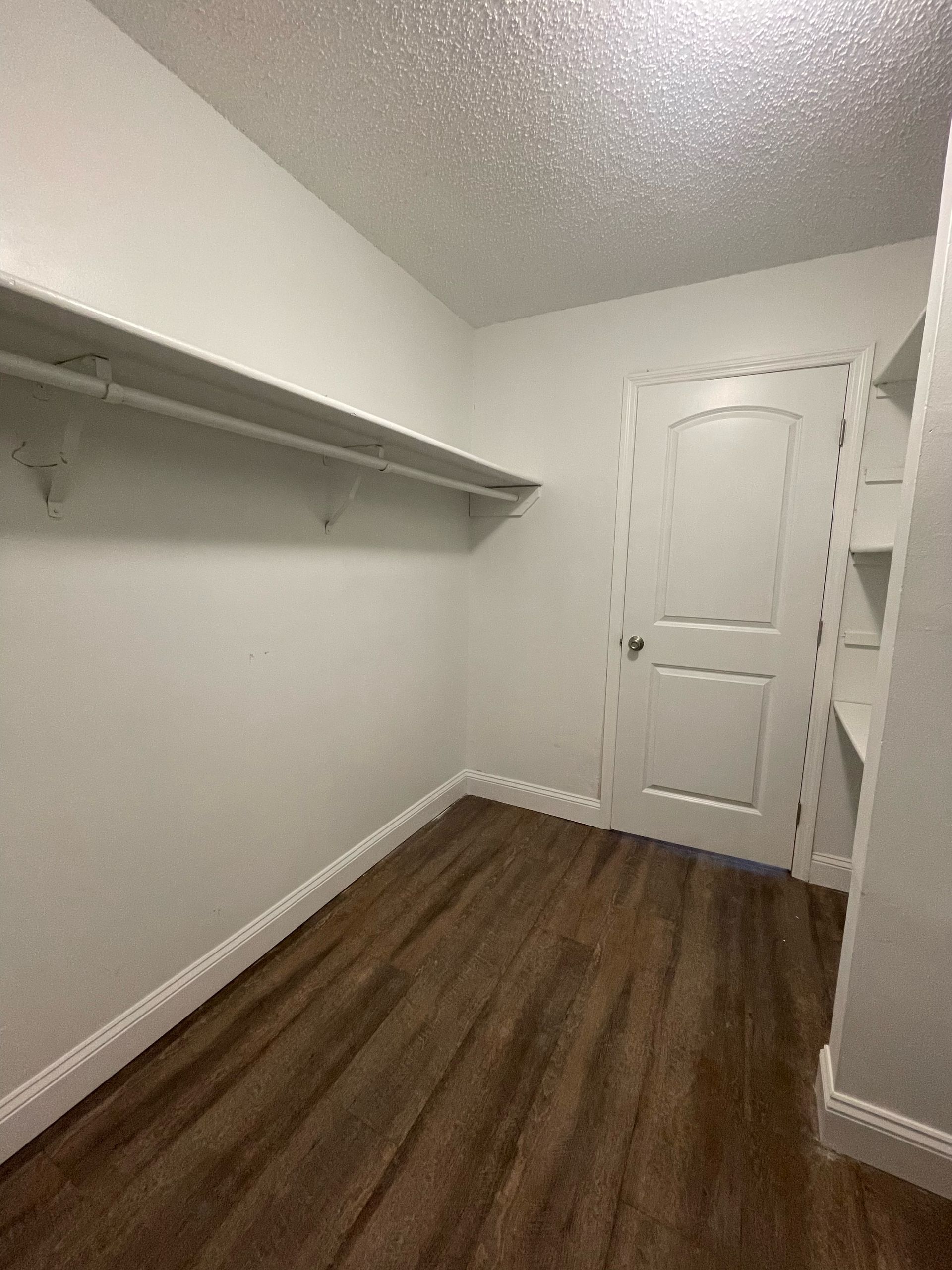 an empty walk in closet with hardwood floors and white walls
