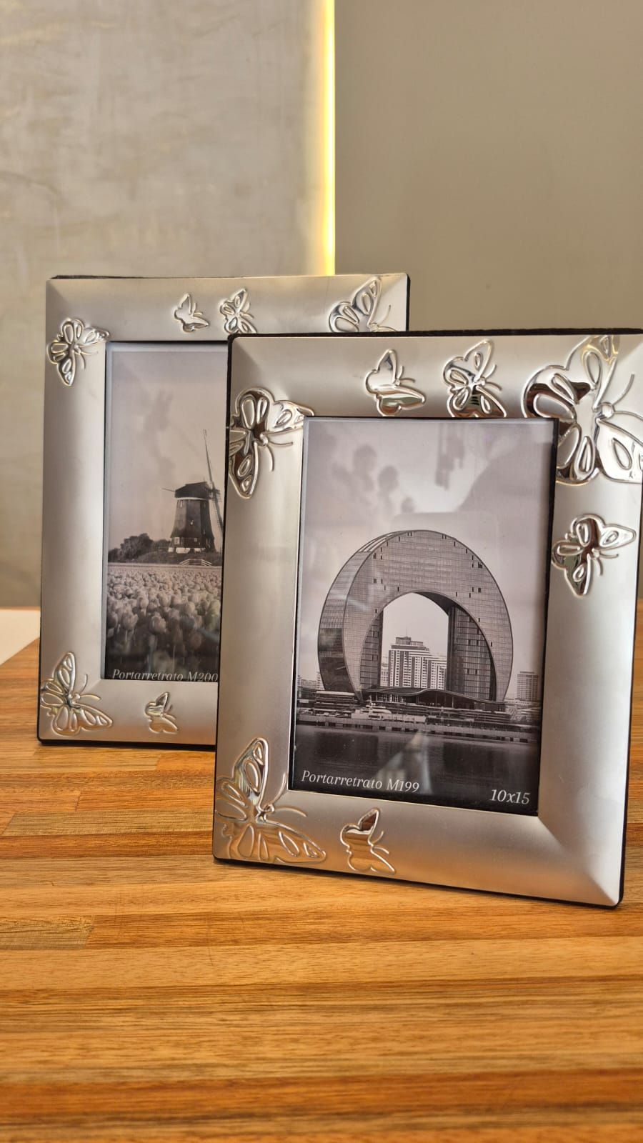 Dos marcos de fotos plateados con motivos florales sobre una mesa de madera.