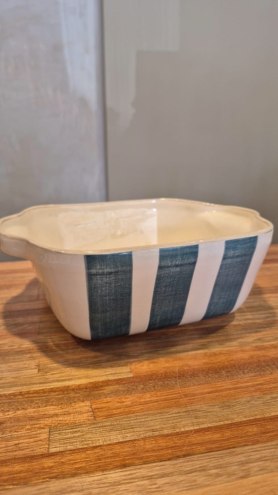 Un pequeño cuenco de cerámica color crema con laterales a rayas azules sobre una mesa de madera.