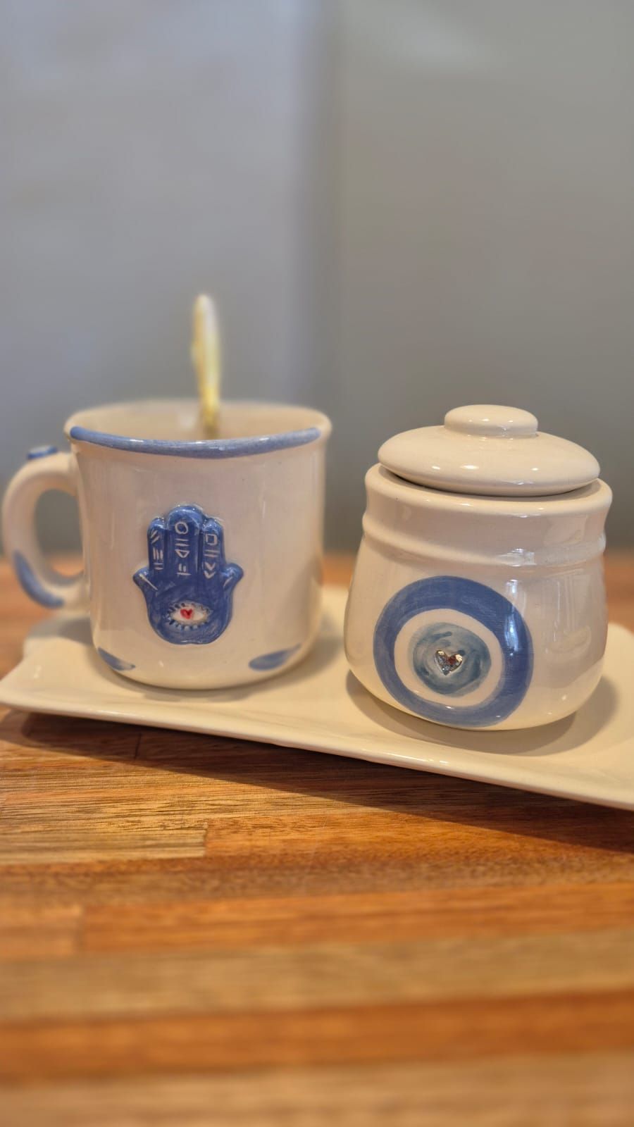 Juego de té en miniatura con una taza azul y blanca, un tarro con tapa y una bandeja sobre una superficie de madera.