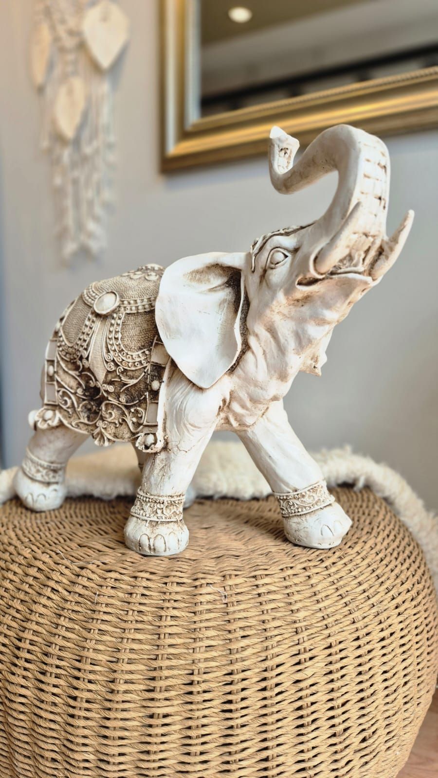 Figura decorativa de elefante blanco sobre un puf tejido en una habitación con iluminación tenue.