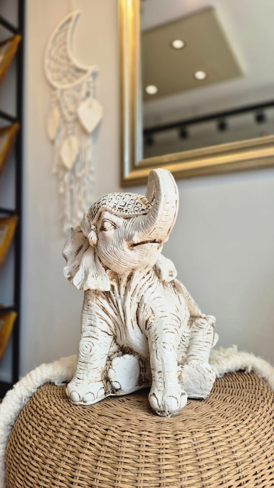 Figura de elefante blanco sobre un taburete tejido junto a un espejo de pared y decoración colgante de macramé.