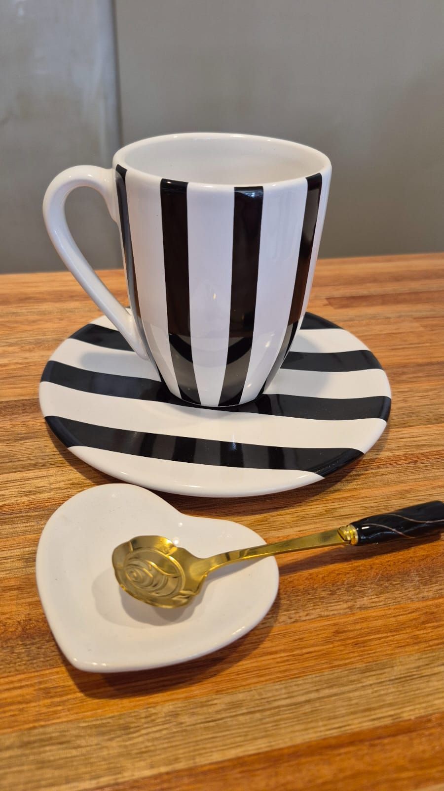 Taza y platillo a rayas blancas y negras con cuchara dorada sobre una mesa de madera.