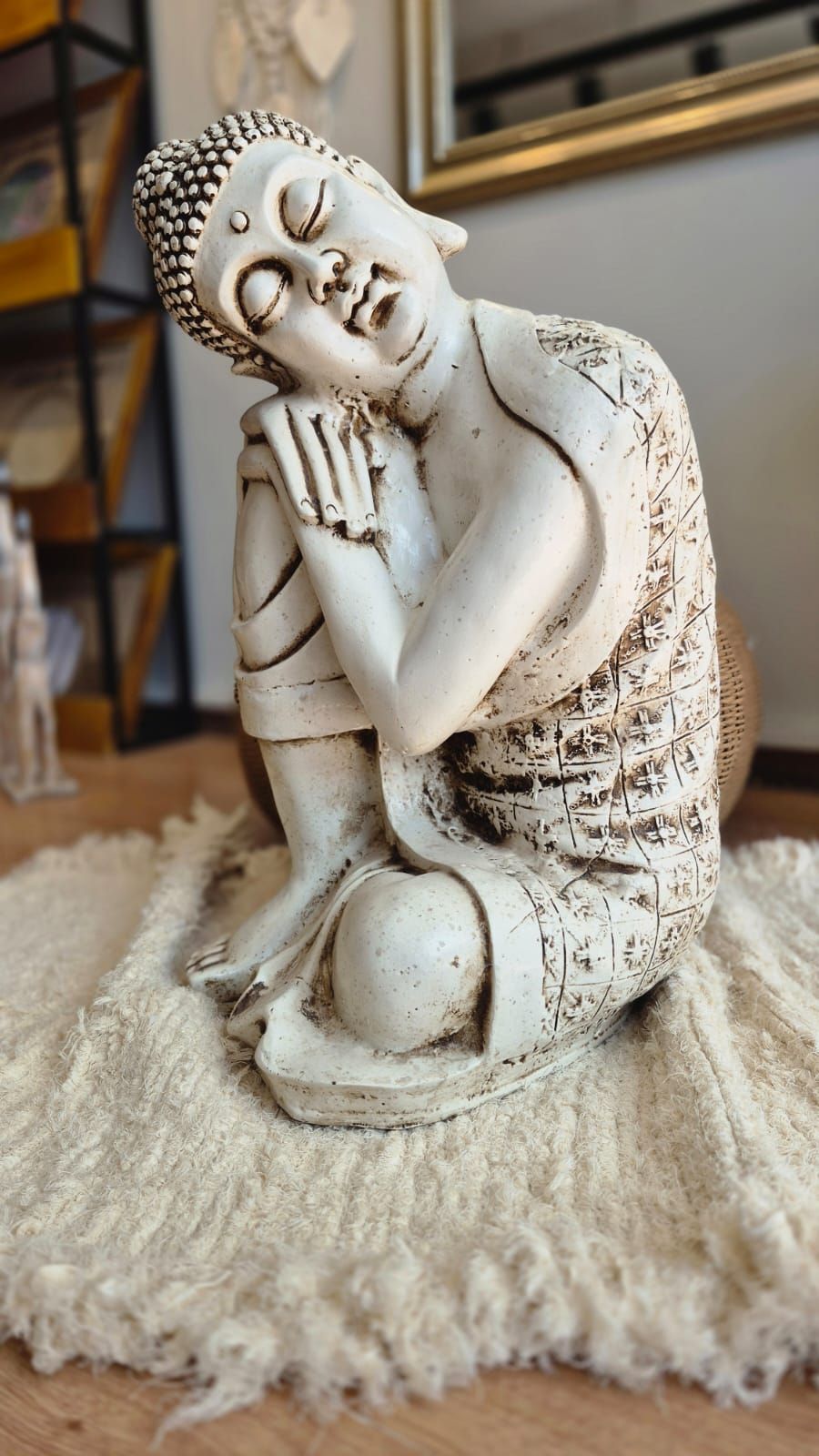 Estatua de Buda blanco con los ojos cerrados, descansando sobre una alfombra beige mullida en el interior.
