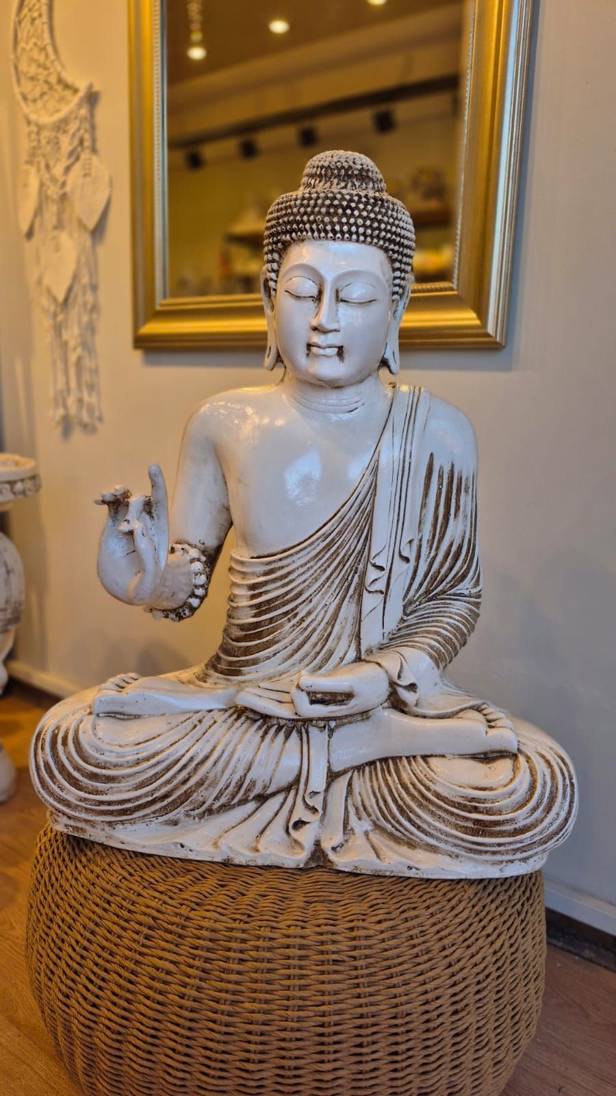 Estatua de Buda blanco sentada sobre un pedestal tejido en un ambiente interior con iluminación cálida.
