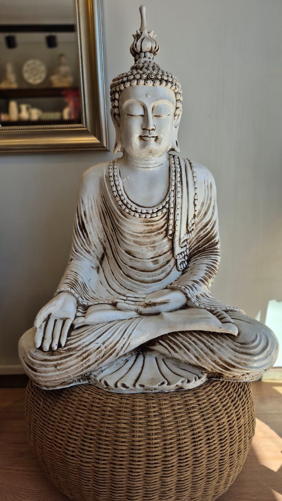 Estatua de Buda blanco sentada sobre un puf tejido contra una pared neutra.