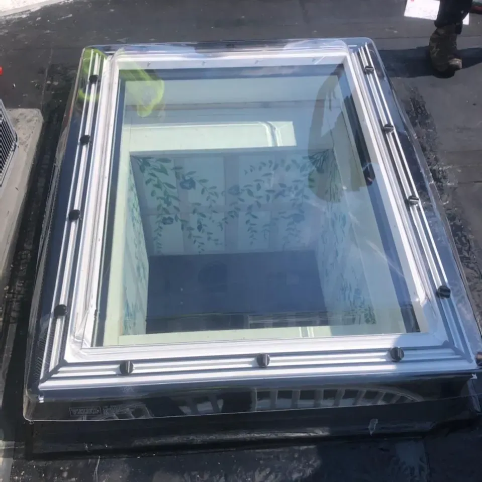 Skylight on a black roof, rectangular with silver trim. Shows interior walls with floral wallpaper.