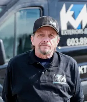 Man in black polo and cap, in front of a van with 