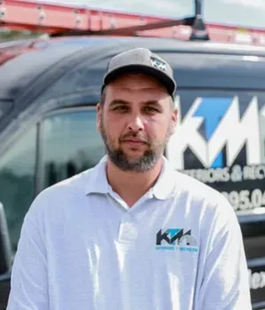 Man in a cap and polo shirt stands in front of a van. 