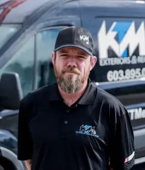 Man in black shirt and cap stands in front of a van with company logo.