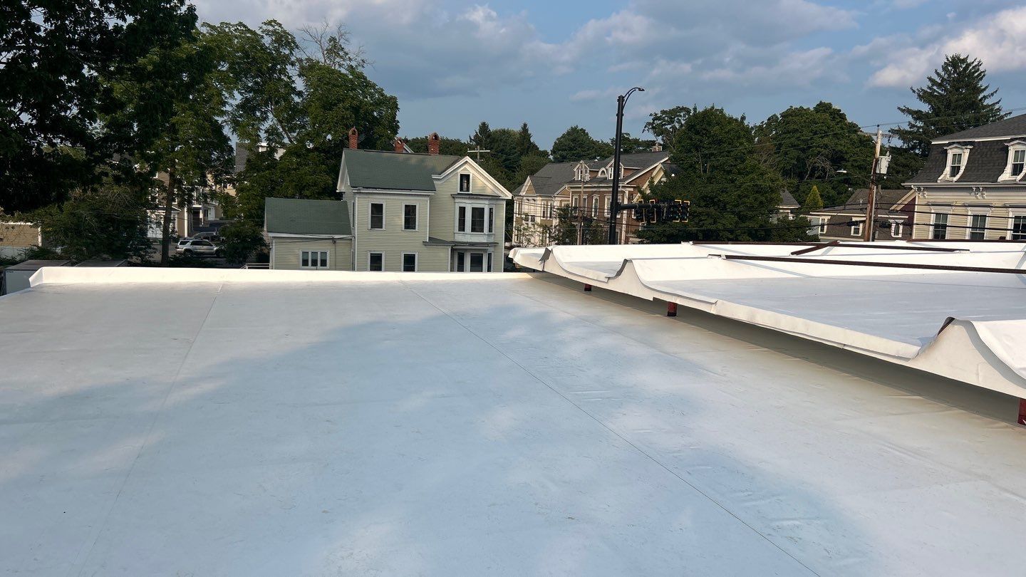White house with black roof, chimney, and trim, blue sky, and green foliage.