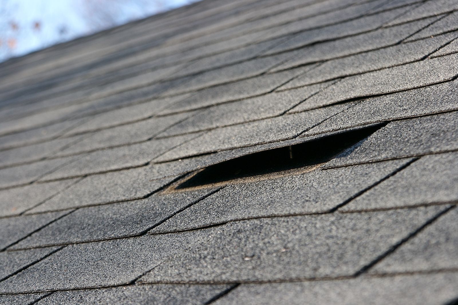 Damaged asphalt shingle roof, with a large rectangular hole.