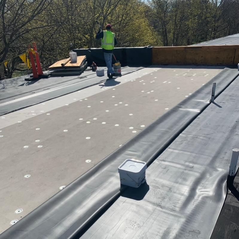 Construction workers installing roofing materials on a flat roof on a sunny day.