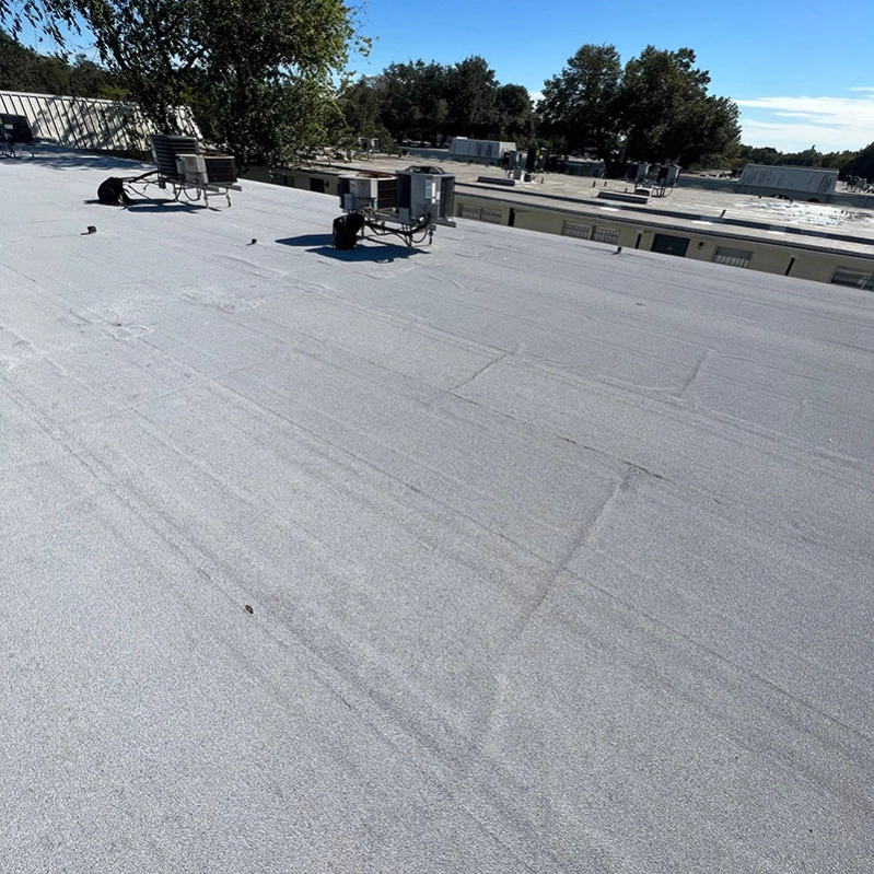 Gray flat commercial roof with HVAC units, against a blue sky.